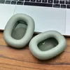 Two green ear pads for headphones are placed on a wooden surface in front of a laptop keyboard. Podgląd zdjęcia produktu