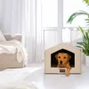 A dog is resting in a dog house indoors, with a couch and plant in the background. Náhled obrázku produktu