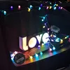 A decorative setup with the word 'love' illuminated by colorful string lights, possibly on a car or a dark surface. Produktbild-Vorschau