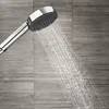 A close-up shot of a modern shower head spraying water against a tiled wall. Produktbild-Vorschau