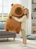 A young girl is hugging a large capybara plush toy in a living room. Produktbild-Vorschau