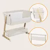 A beige and white baby bassinet with a storage shelf underneath, shown on a light gray background. Inset images highlight adjustable height settings and a side view of the bassinet. Produktbild-Vorschau