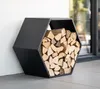 A black hexagonal firewood rack filled with logs, placed on a patio next to a white wall. Podgląd zdjęcia produktu