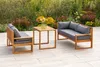 Outdoor patio furniture set with a sofa, chair, and table, set against a backdrop of blooming flowers. Produktbild-Vorschau