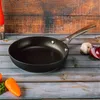 A frying pan is placed on a wooden table with some vegetables and a salt grinder in the background. Náhľad obrázku produktu