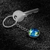 A silver key with a keychain featuring a miniature globe of Earth rests on a dark, textured surface. Podgląd zdjęcia produktu