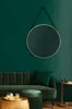 A round mirror with a gold frame hangs on a dark green wall above a green velvet sofa. A green ottoman and a gold coffee table with drinks are in the foreground. Náhled obrázku produktu