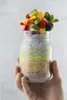 A hand holding a mason jar filled with layered chia pudding and topped with fresh fruit. Voir les images du produit