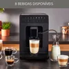 A black KRUPS automatic espresso and cappuccino machine is shown on a countertop, with several cups of coffee and a carafe of milk nearby. The machine is in operation, with a stream of milk pouring into a glass. Voir les images du produit