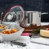 A cooking pot and a bowl of pasta are arranged on a table with ingredients like cheese and herbs. Anteprima dell’immagine prodotto