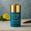 A Versace Eros perfumed deodorant stick is displayed on a wooden surface with a slice of lemon and mint leaves in the background. Podgląd zdjęcia produktu