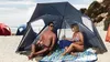 Two people relaxing under a beach tent on a sandy beach. Voir les images du produit