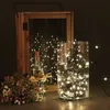 A decorative arrangement of fairy lights in a glass vase and a wooden lantern, with a small bouquet of flowers. Produktbild-Vorschau