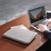 A person's hands are typing on a laptop, with a laptop sleeve and magazines on a wooden desk. Produktbild-Vorschau