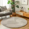 A circular rug with a geometric pattern is placed on a wooden floor in a living room setting, next to a gray sofa and a wooden cabinet. Voir les images du produit