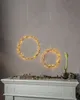 Two LED light wreaths are hanging above a white mantelpiece decorated with greenery and books. Podgląd zdjęcia produktu