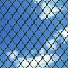 A chain-link fence against a blue sky with clouds. Produktbild-Vorschau