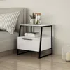 A modern white nightstand with black metal legs is placed next to a bed. Produktbild-Vorschau