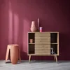 A modern Scandinavian-style sideboard with a ribbed sliding door, displayed in a room with a deep pink wall and a terracotta stool. Anteprima dell’immagine prodotto