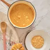 A top-down view of a cast iron pan filled with a creamy orange dish, next to a bowl of the same dish, with a wooden spoon and a napkin. Produktbild-Vorschau