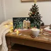 A festive Christmas scene with an advent calendar, a small Christmas tree, and a mug of hot chocolate on a wooden table. Produktbild-Vorschau