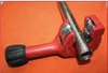 A red pipe cutter is shown on an orange surface, with a metal pipe inserted into it. Anteprima dell’immagine prodotto