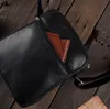 A close-up view of a black leather bag with a brown wallet peeking out of a zippered pocket, resting on a wooden surface. Podgląd zdjęcia produktu