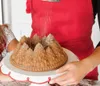 A person is dusting a bundt cake shaped like a pine forest with powdered sugar. Anteprima dell’immagine prodotto
