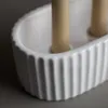 A close-up shot of a white ceramic candle holder with two beige candles inside. Produktbild-Vorschau