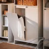 A white cabinet with a laundry basket and clothes inside, in a room with a brown rug. Náhled obrázku produktu