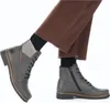 A close-up shot of two grey boots worn with brown pants and black socks. Náhled obrázku produktu