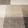 A close-up view of a carpet with a checkered pattern in various shades of beige and gray. Produktbild-Vorschau