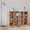 A modern living room or office space with a concrete wall and wooden floor, featuring a set of wooden bookshelves filled with decorative items and books, alongside a floor lamp and a table lamp. Produktbild-Vorschau