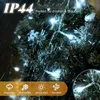 A close-up of white LED string lights on a dark green, possibly artificial, Christmas tree, with simulated rain falling. Náhled obrázku produktu