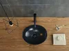 A top-down view of a black ceramic washbasin on a wooden countertop, with a modern pendant light and bathroom accessories. Náhľad obrázku produktu