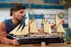 A man is shown assembling a detailed model of a sailing ship. Voir les images du produit