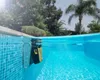 A pool cleaning robot is shown partially submerged in a swimming pool, cleaning the tiled wall. Produktbild-Vorschau