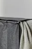 A close-up view of the top of a grey laundry basket with a white waffle-weave blanket draped over the side. Produktbild-Vorschau