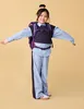 A young girl wearing a backpack and school uniform stands with her arms outstretched against a plain background. Produktbild-Vorschau
