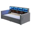 A grey upholstered daybed with a built-in bookshelf headboard featuring blue LED lighting and two storage drawers underneath. Náhled obrázku produktu