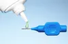 A close-up shot of a blue TePe interdental brush with a drop of green gel being dispensed onto it from a white bottle. Produktbild-Vorschau