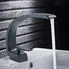 A black modern faucet is shown in use, with water flowing into a white sink. The background is a textured gray wall. Podgląd zdjęcia produktu