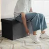 A person is sitting on a dark gray storage ottoman. Anteprima dell’immagine prodotto