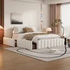 A bedroom scene featuring a beige upholstered bed with open storage drawers, a rug, and decorative elements. Produktbild-Vorschau