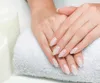 A pair of hands with manicured nails resting on a white towel, with two white candles in the background. Náhled obrázku produktu