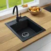 A black kitchen sink with a faucet is shown on a wooden countertop, with a window and fruit in the background. Produktbild-Vorschau