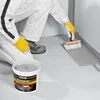 A person is applying a waterproofing liquid with a brush to the corner of a floor and wall. Produktbild-Vorschau