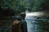 A person wearing a headlamp and backpack stands by a river in a forest. Podgląd zdjęcia produktu