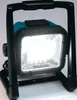 A portable LED work light with a black frame and turquoise body, illuminated and standing on its base. Podgląd zdjęcia produktu