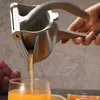 A hand is using a manual juicer to squeeze juice into a glass. Grapes and citrus fruits are visible in the background. Produktbild-Vorschau